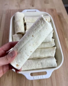 This is a picture of a breakfast burrito in hand in front of a pile of burritos.
